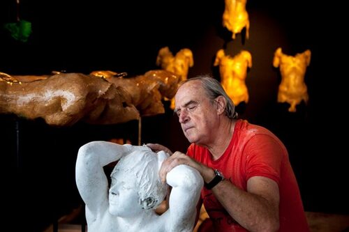 MICHAEL IN HIS STUDIO WORKING ON A SCULPTURE WITH A NUMBER OF SCULPTURES BEHIND HIM.